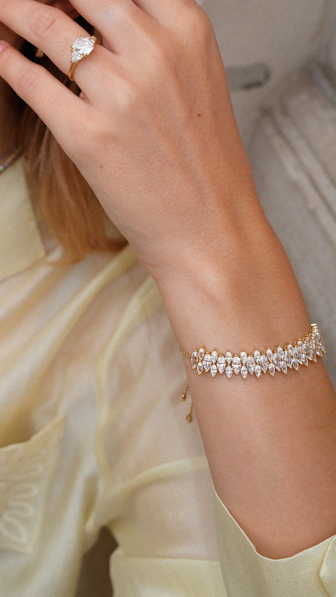 Close-up of a hand wearing a diamond style ring and marquise gemstone adjustable tennis bracelet in gold.